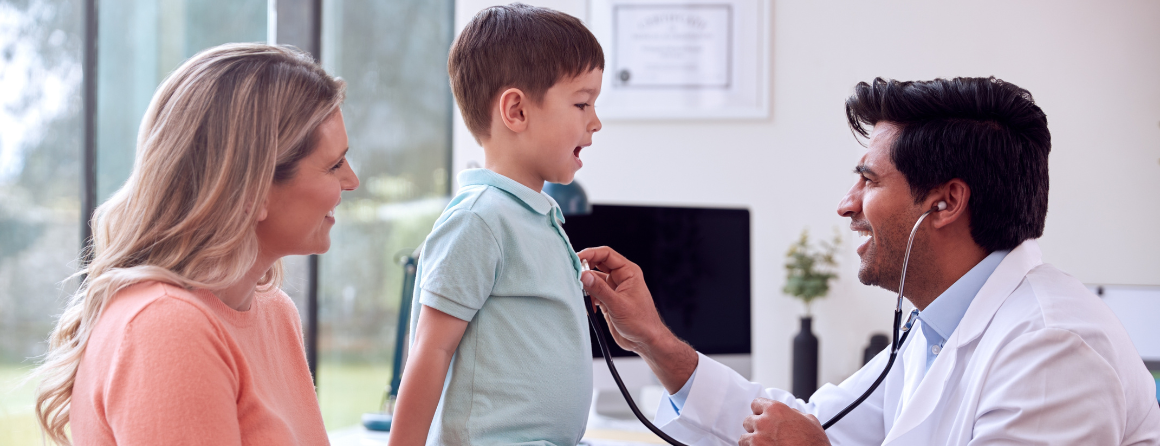 GP In White Coat Meeting Mother And Son For Appointment In clinic listening To Chest