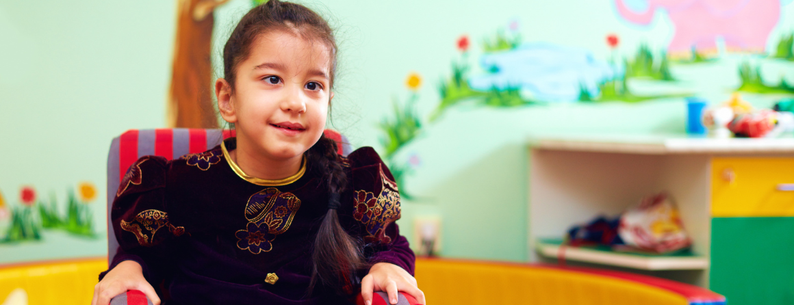 Smiling girl with neurodevelopmental disorder in a playroom sitting on a chair 