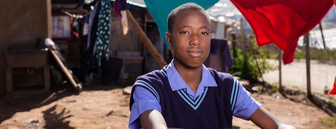 A boy leans on a fence in a rural setting