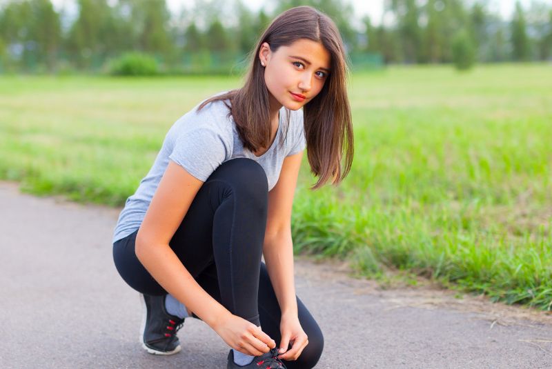 Athletic teenage girl in park lacing up her shoelaces 