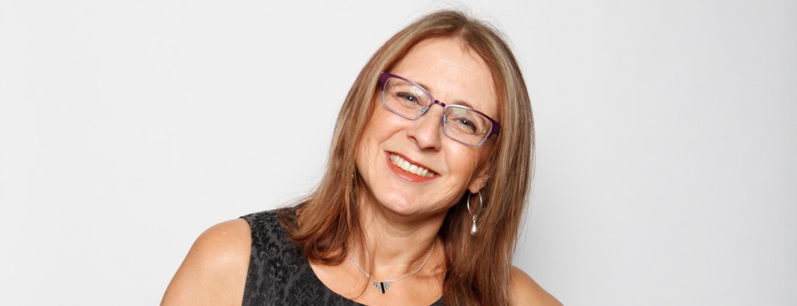 A researcher with light brown hair and glasses smiles at the camera in front of a plain, off-white backdrop.