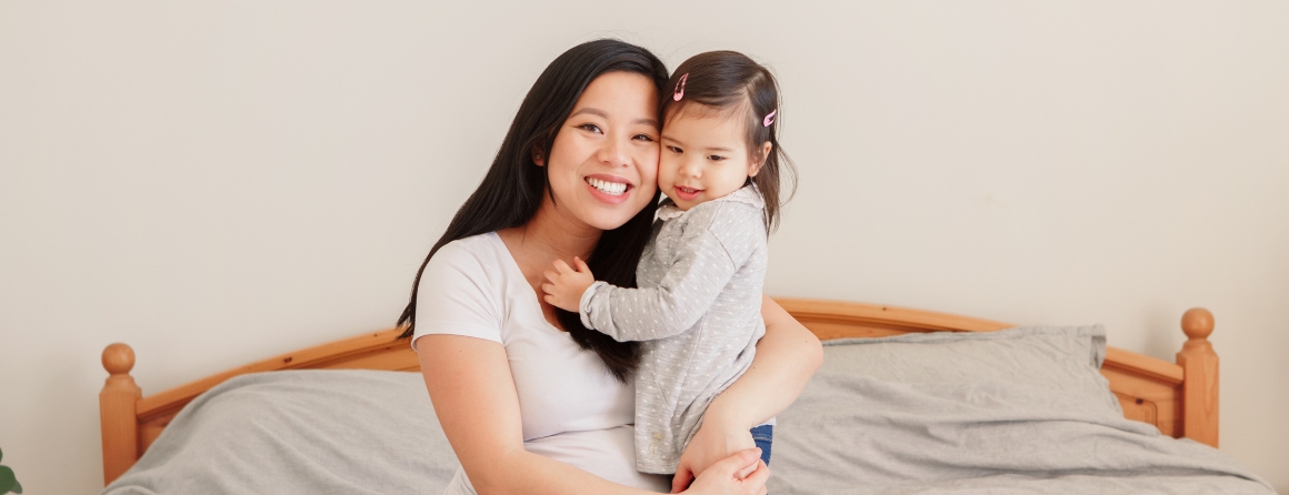 A pregnant mother hugging a toddler on a bed