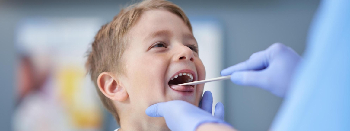 Cheerful boy getting throat examination from doctor 