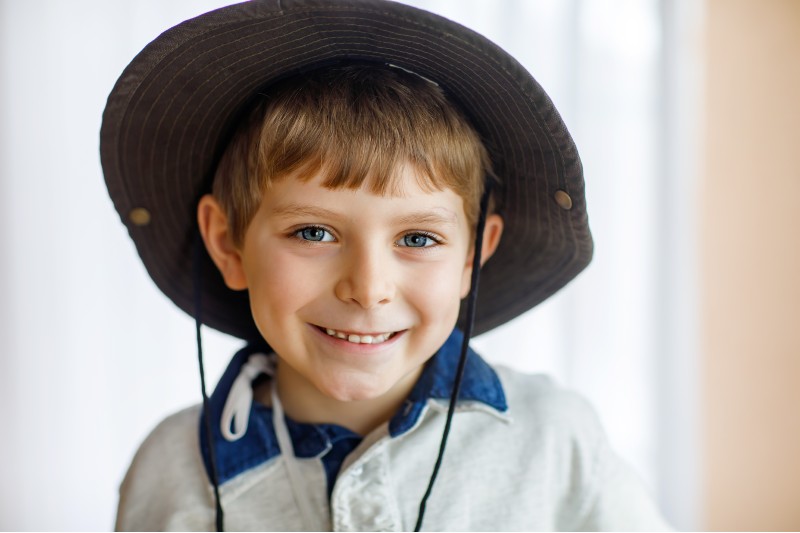 A primary-school aged boy weaing his uniform and a broad-rimmed hat.