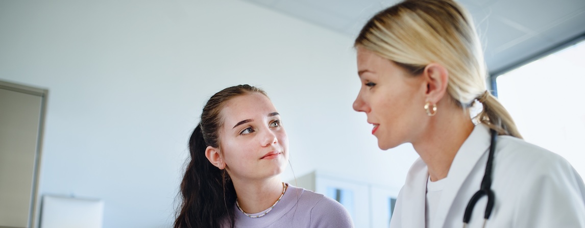 A doctor shows medical notes to a patient, who is a young woman with long, dark hair. 