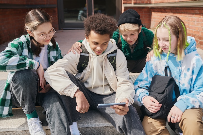 4 teenagers looking at a social media site on a phone