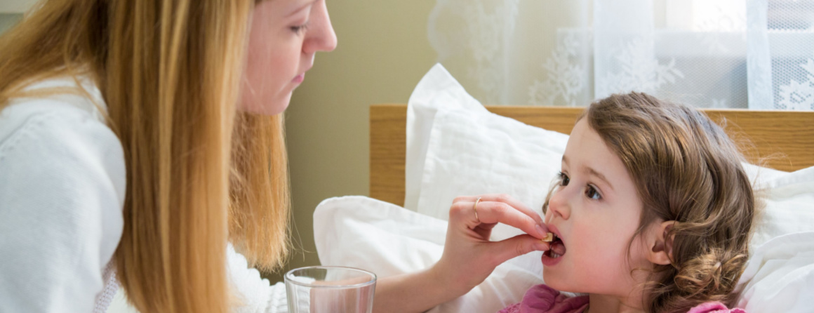 Worried mother giving glass of water to her ill kid. Sick child with high fever laying in bed and taking a medicine. Hand on forehead