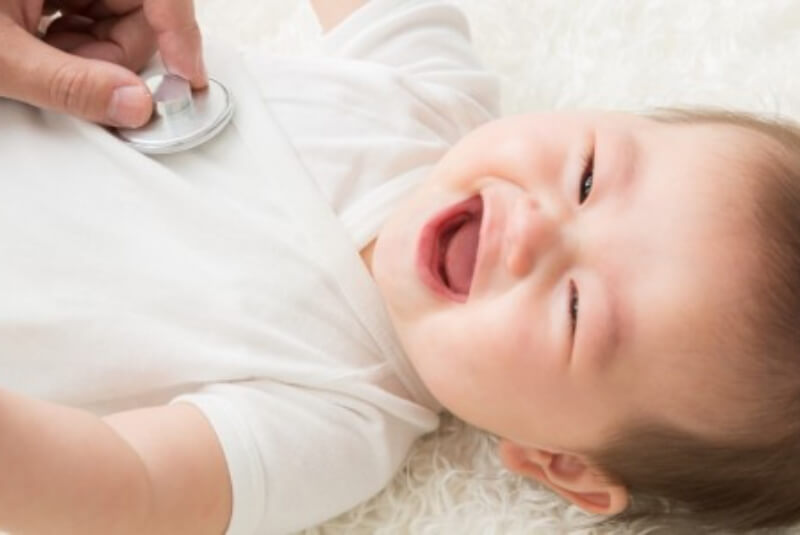 Person using a stethoscope on the chest of a laughing infant.