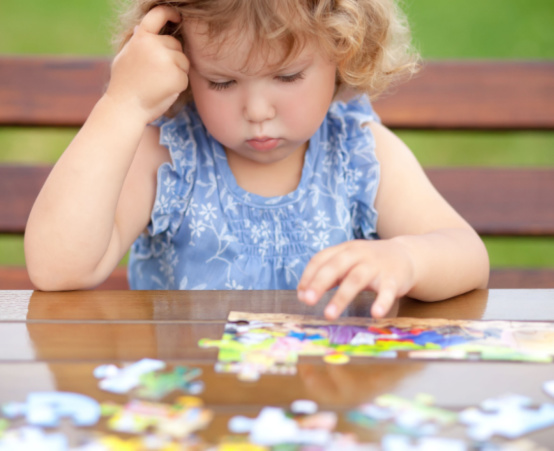 Little girl with blonde curly hair having trouble with a puzzle