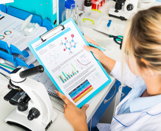 Researcher in lab reviewing documents in front of microscope