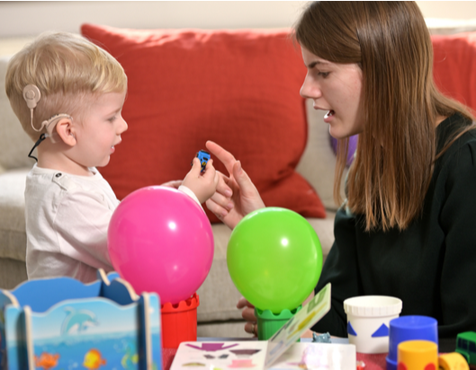 Little boy with hearing aid speaks to therapist