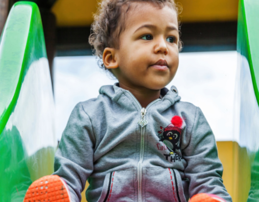 Little boy sitting at the top of green slide in a playground
