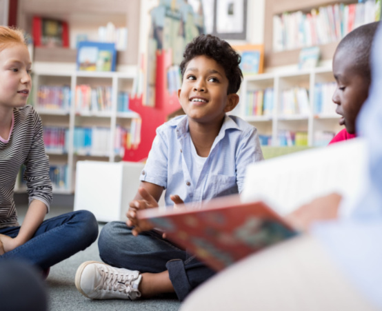 Teacher reading a book to young children at school sitting on a mat