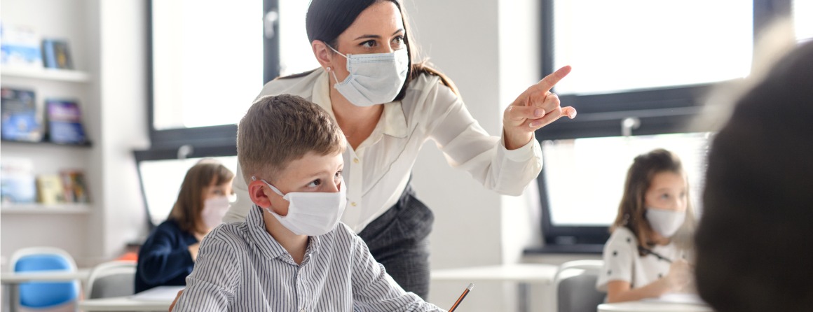 A child in school with a teacher, both wearing masks