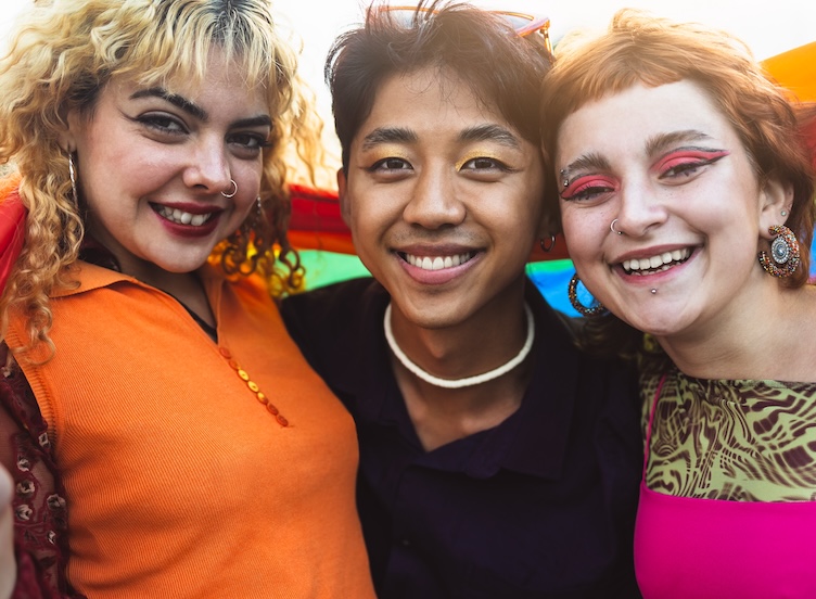 3 LGBTQIA+ persons arm in arm holding a pride flag
