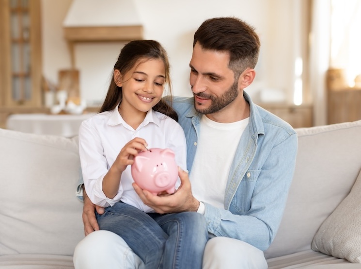 A child puts money in a piggy bank with her father
