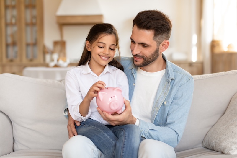 A child puts money in a piggy bank with her father